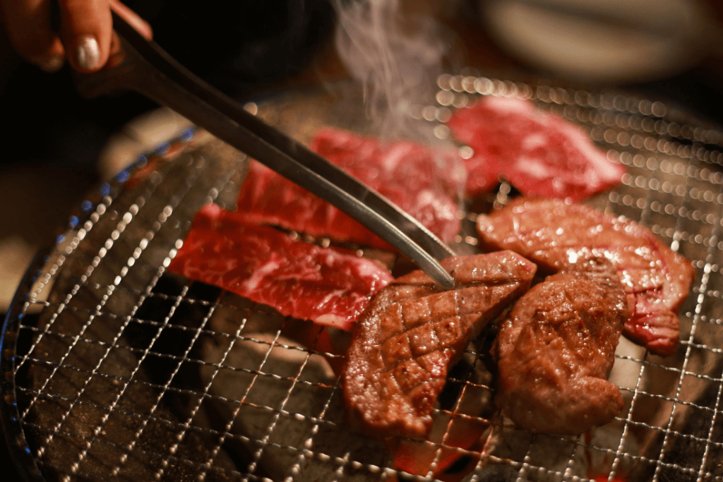 Grilled meat, or yakiniku being cooked on a grill. People serve it with takoyaki.