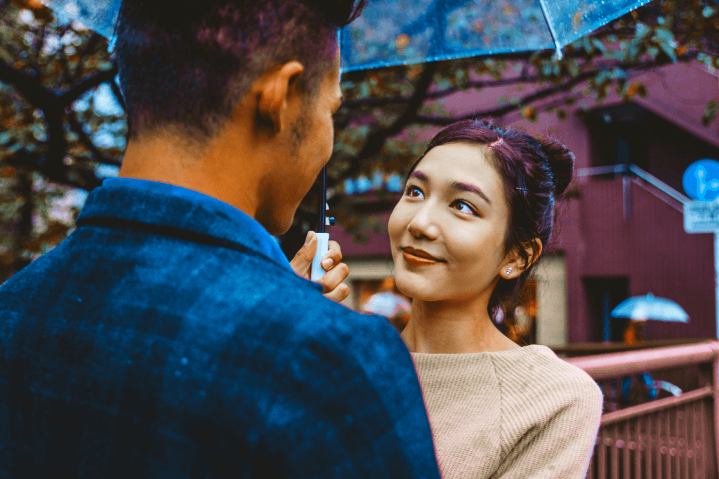 A woman lovingly looking at a man under an umbrella.