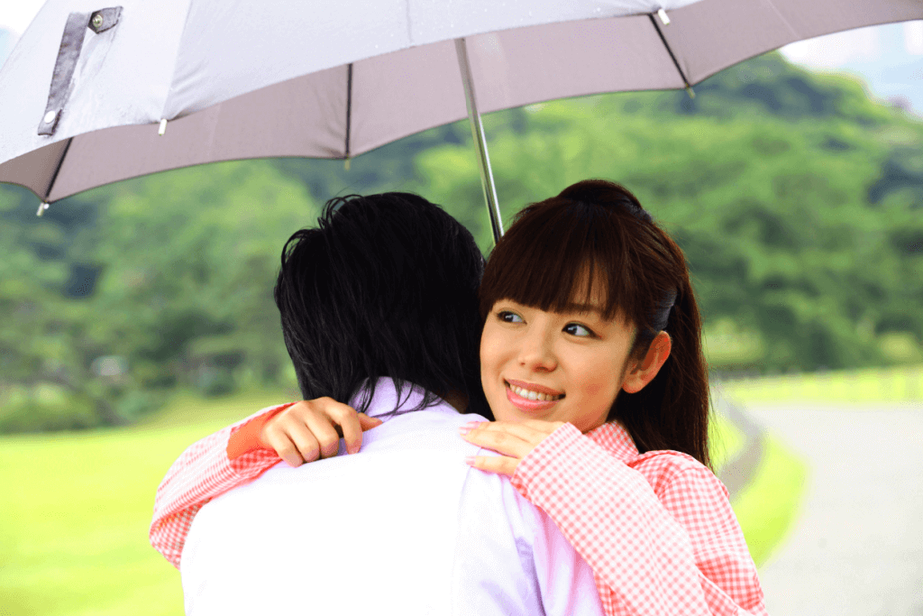 A woman hugs a man under an umbrella, most likely practicing how to say I love you in Japanese.