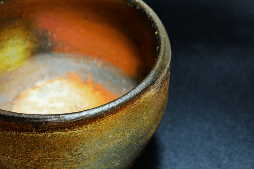 A green brown bizen yaki bowl against a background. It almost looks like it's glowing.