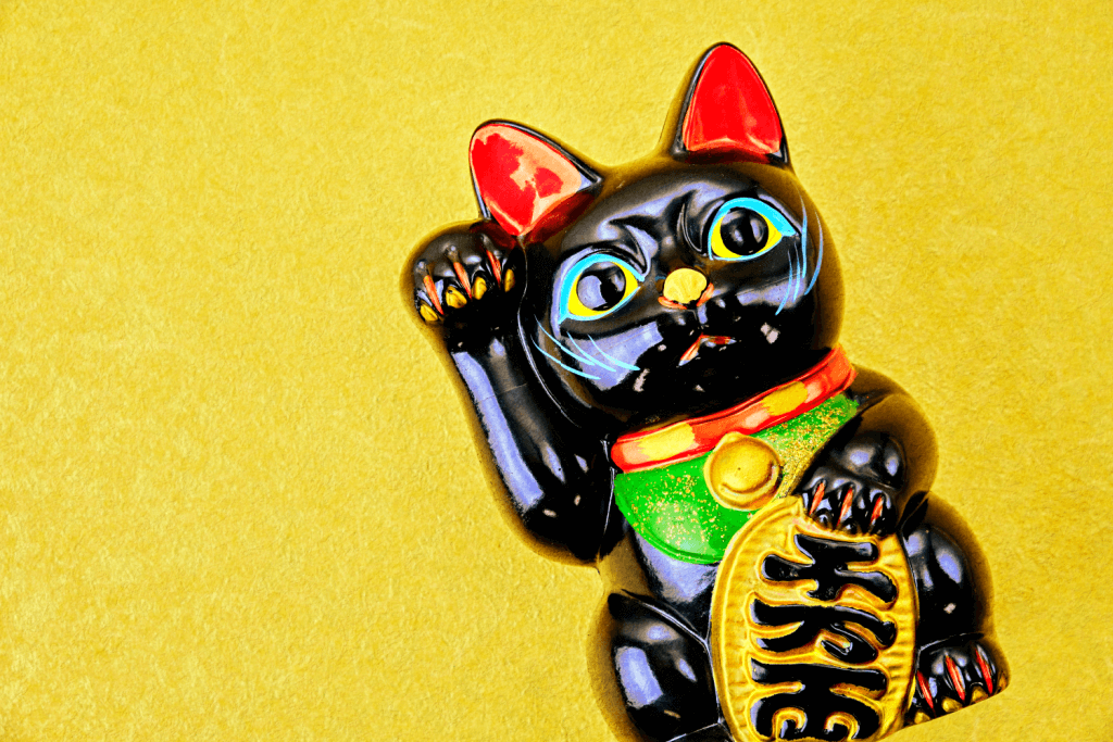 A black maneki neko statue with a raised left paw against a yellow background.