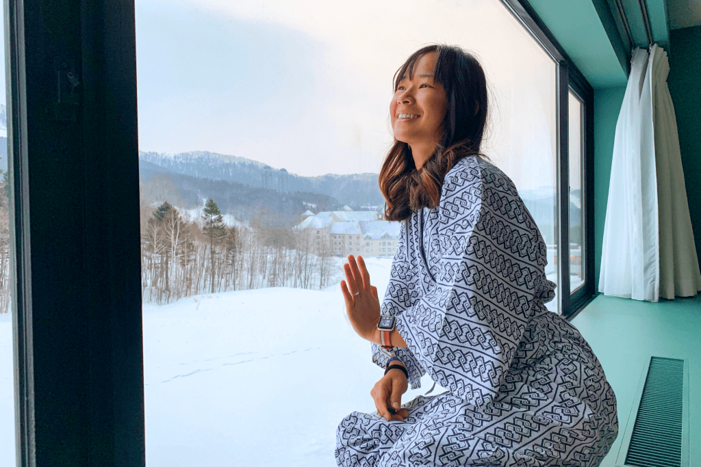 A woman wearing jinbei pajamas, smiling as she looks out the window.