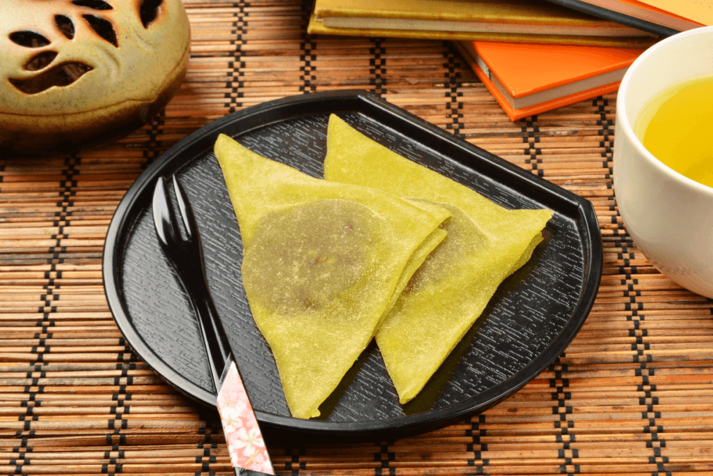 A plate of nama yatsuhashi with red bean paste inside. They are triangle shaped, and green tea.