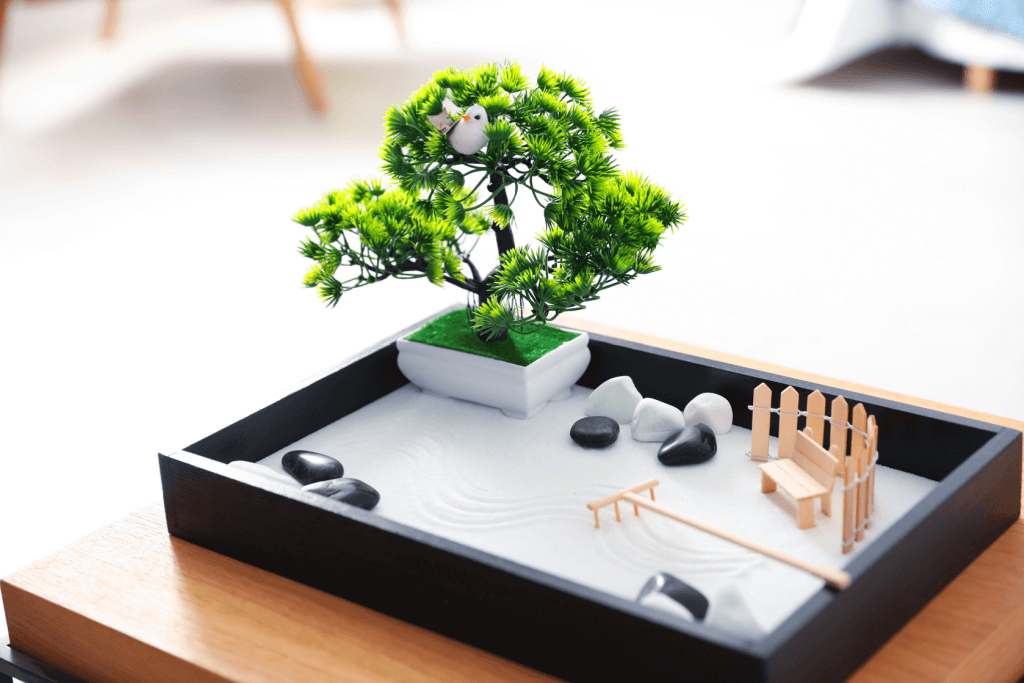 A mini garden with bonsai, light gray gravel and a small rake.