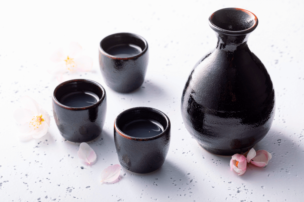 A bunch of black, glazed sake cups with sakura flowers on the side.
