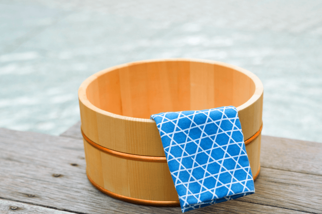 A light blue Japanese tenugui towel in a wooden bucket, one of many popular traditional Japanese gifts.