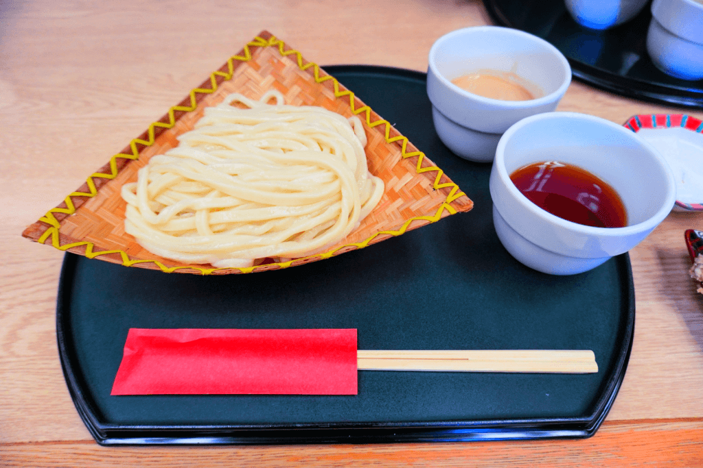 A plate of Mizusawa Udon, (thick, firm noodles) with chopsticks and tsuyu on the side.