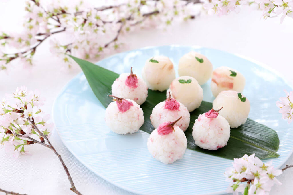 Temari sushi for cherry blossom viewing party on pale blue plate. They include salty pickled cherry blossoms.
