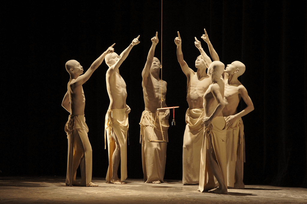 A bunch of butoh dancers on stage in all white, with their hands raised.