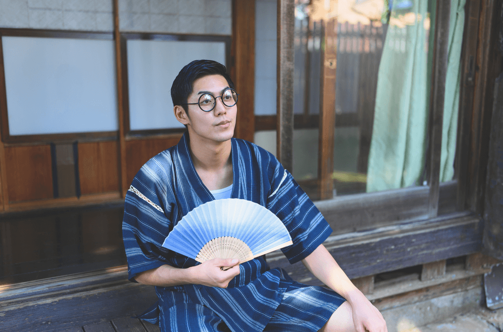 A man wearing jinbei clothing while fanning himself on the summer porch.