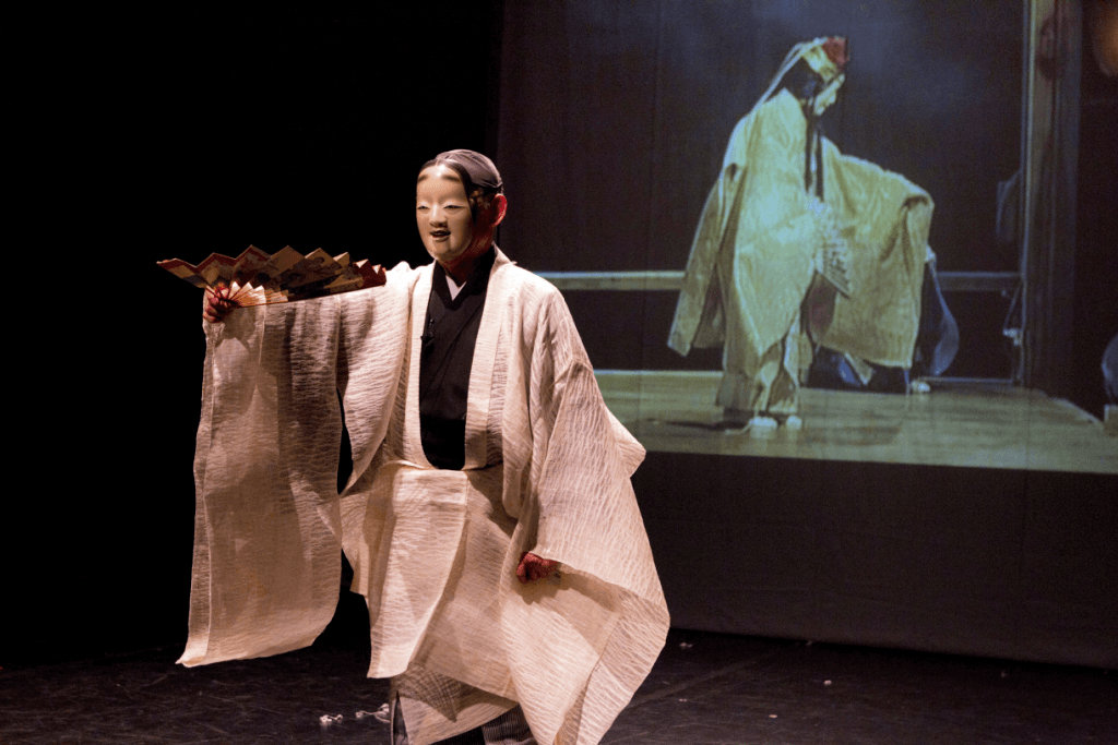 A person in a Noh theater mask, performing for the crowd.