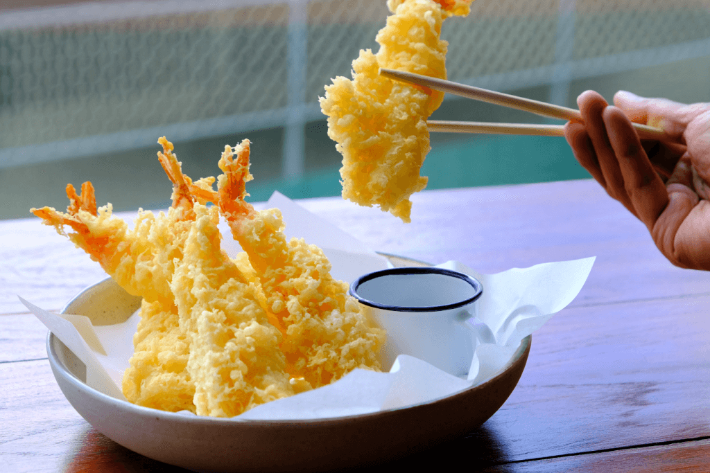 A plate of fish and shrimp tempura with chopsticks.
