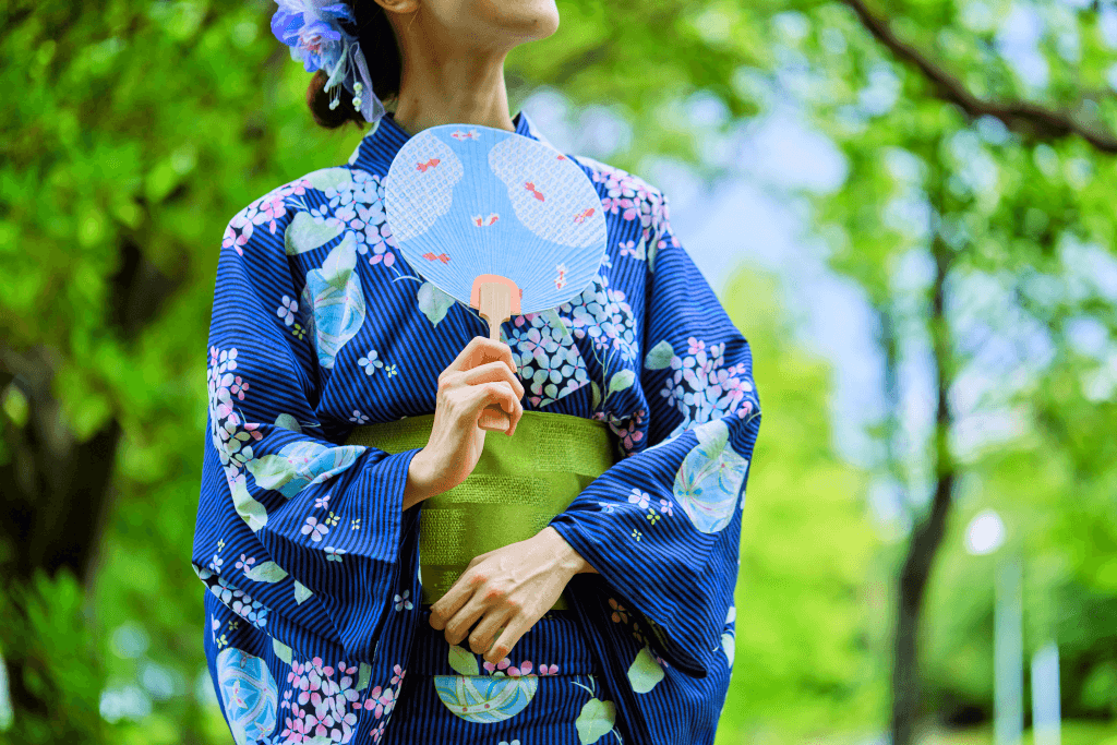 A woman wearing an indigo blue yukata while holding a blue uchiwa fan.
