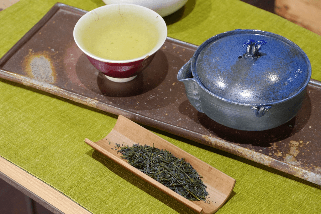 A cup of shincha next to tea leaves and a teapot.
