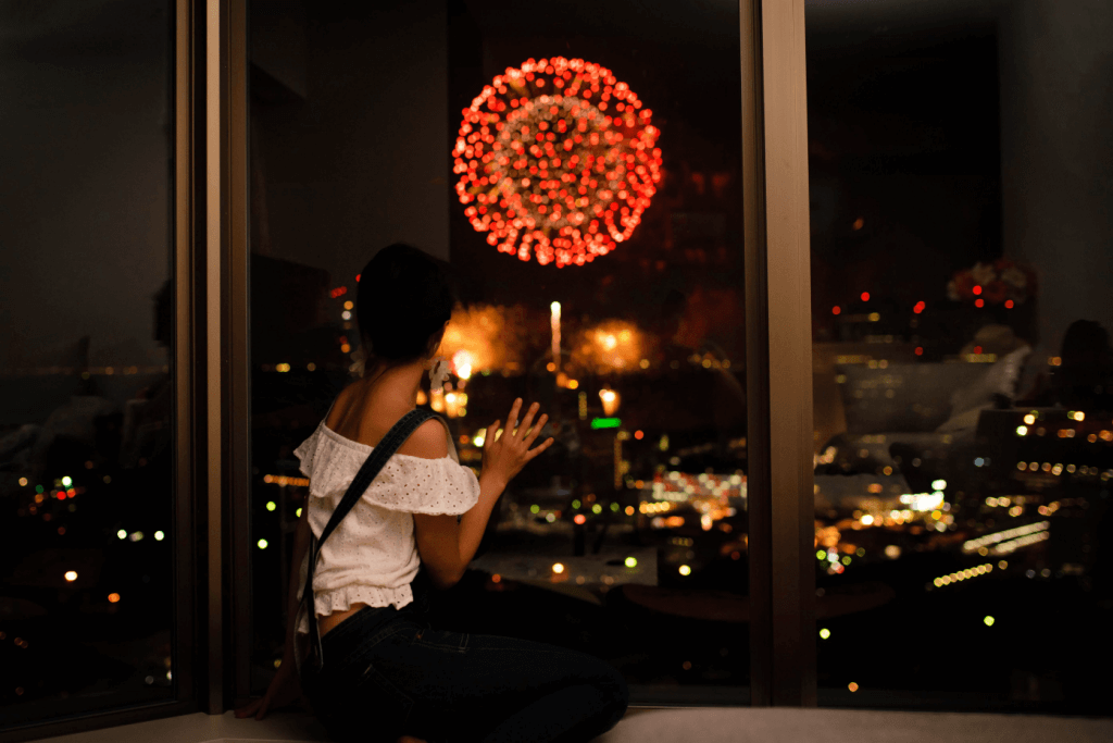 A woman sitting at her window observing a large, red firework.