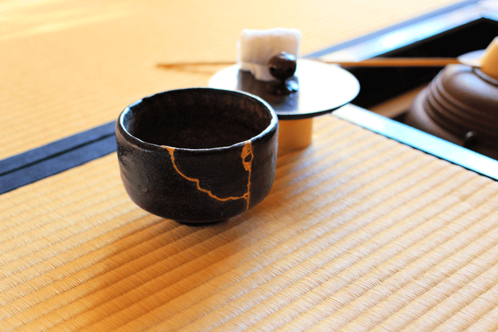 A black kintsugi pottery bowl on a tatami mat.