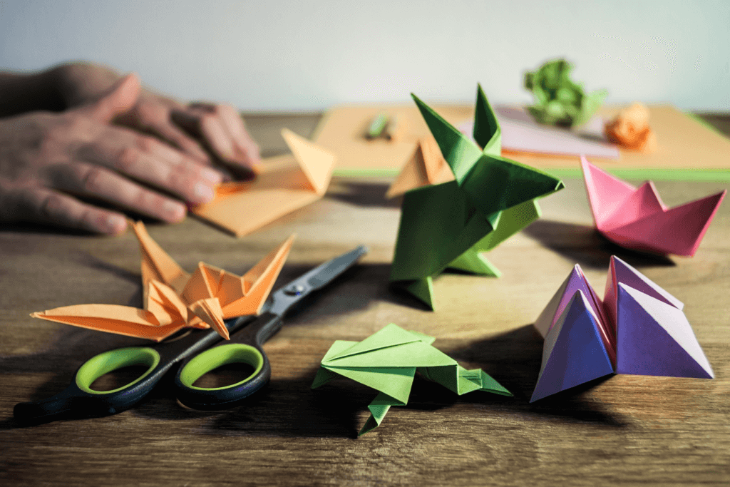 People folding up origami paper in the shape of cranes, purple and green.