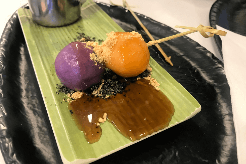 A plate of purple and yellow dango on a skewer.