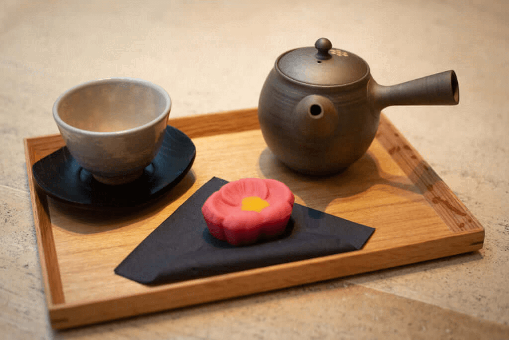 A red flower namagashi with tea on a plate.