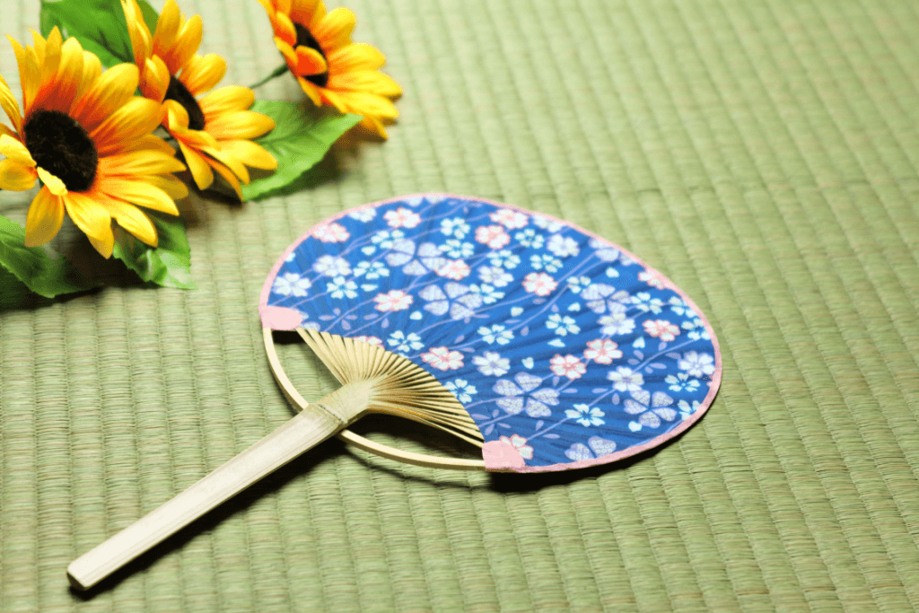 A bo shu style uchiwa fan. It's blue with a floral pattern and resting on a green tatami mat.