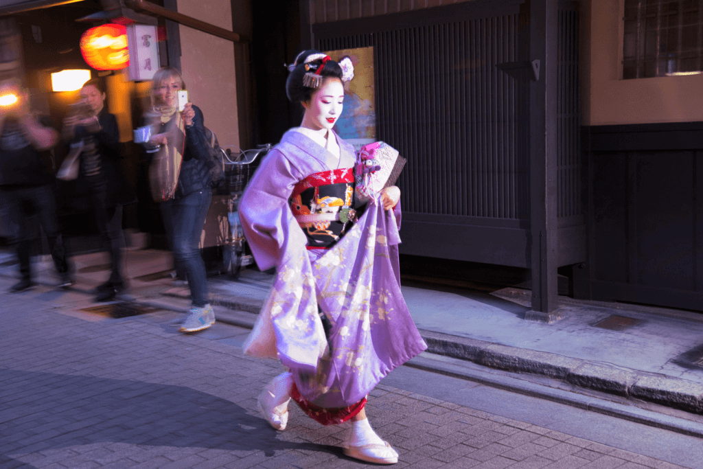 A geisha in a purple kimono walking through the streets of Kyoto.
