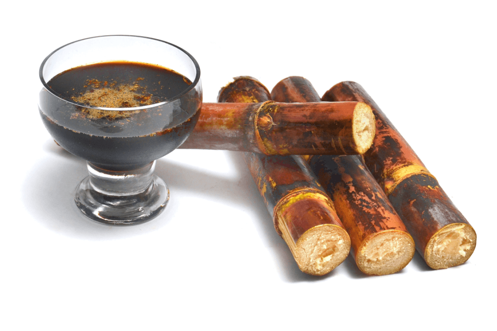 A glass of kuromitsu syrup next to toasted sugar cane.