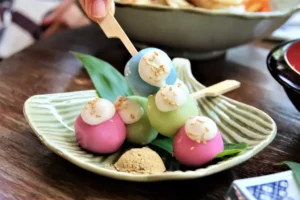 Three dango skewers of pink, green and blue with whipped cream and sesame seeds on top.