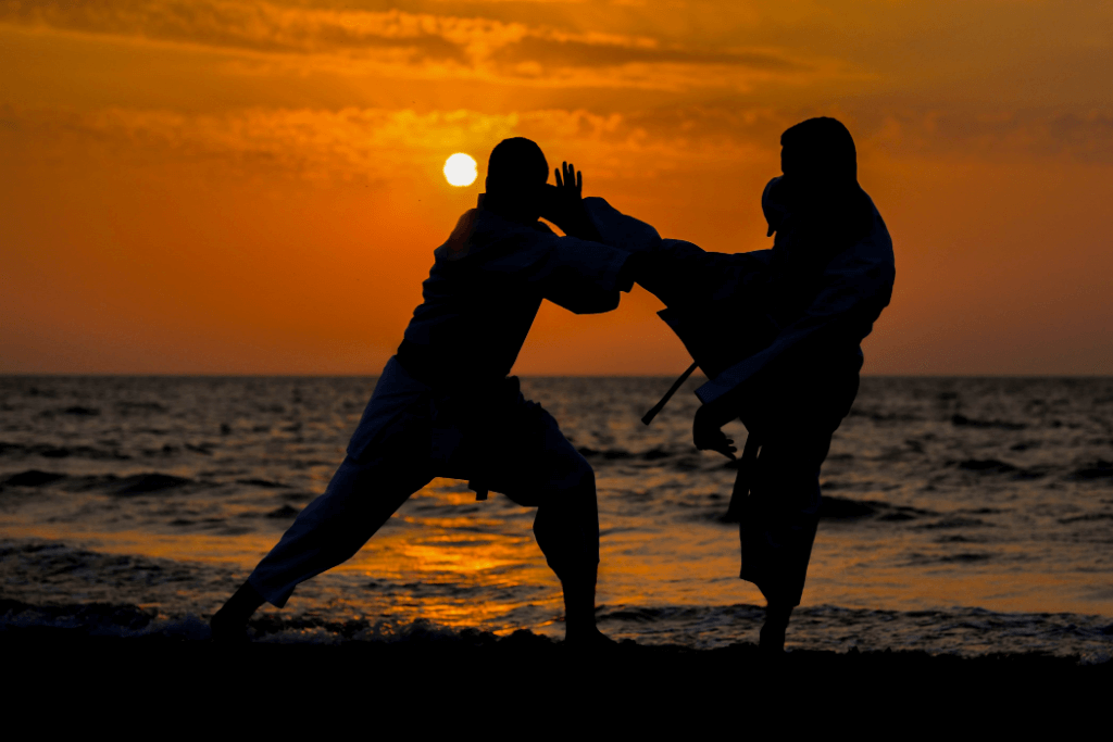 Two people practicing Okinawan martial arts on the beach at sunset.