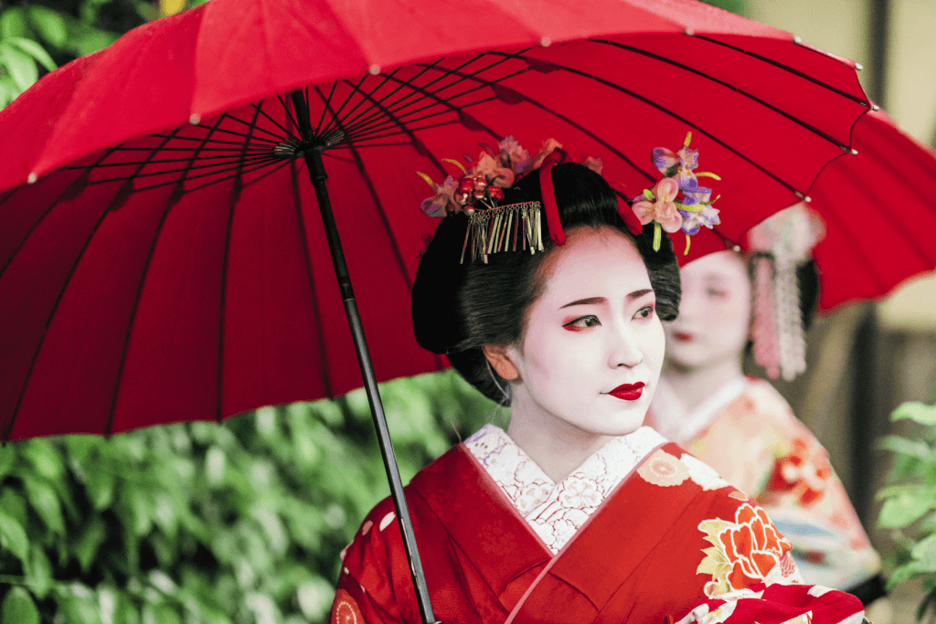 A geisha with white face paint and a red kimono.
