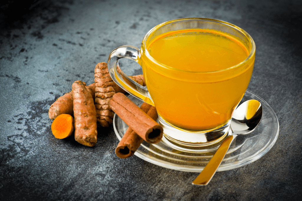 A cup of turmeric tea with turmeric root on the side. They are both orange.