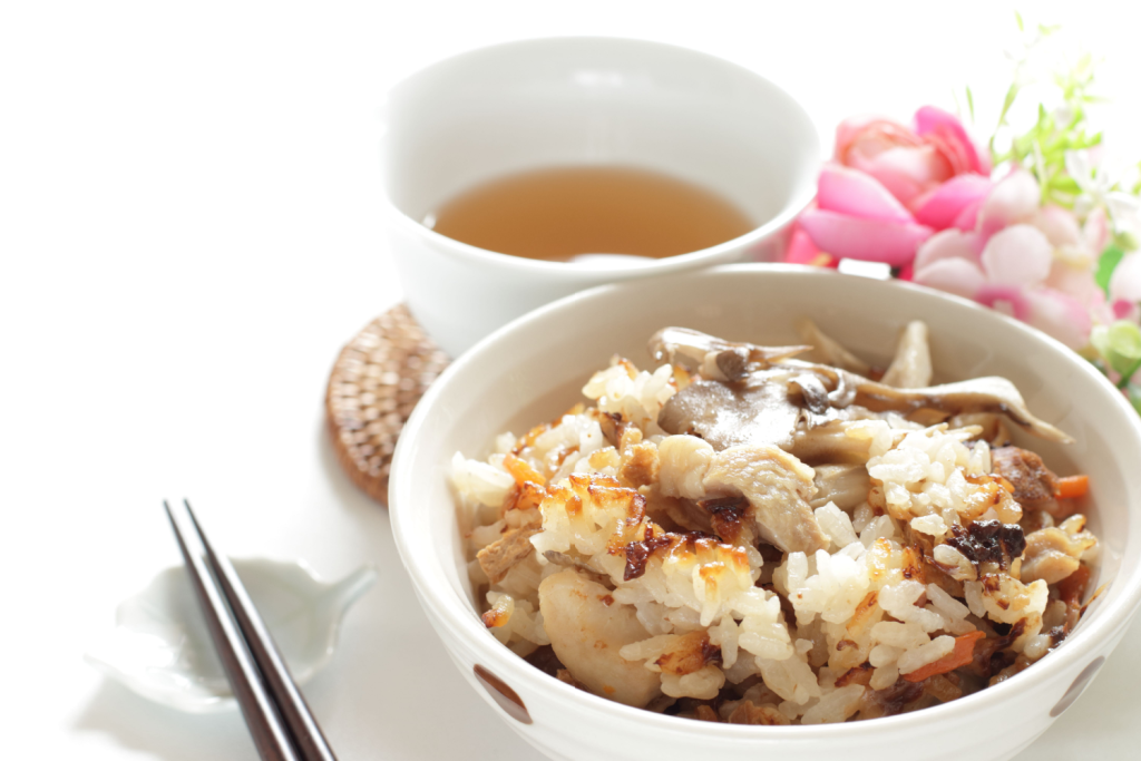 An bowl of okoge, chicken, and miitake mushrooms sits next to a cup of tea.