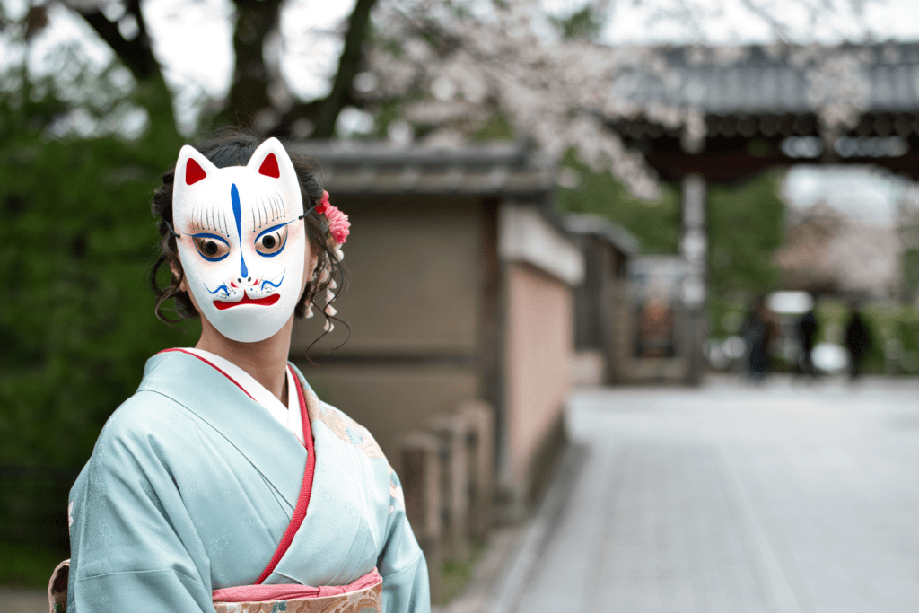 A young woman is wearing a Japanese traditional kitsune mask at a shrine.