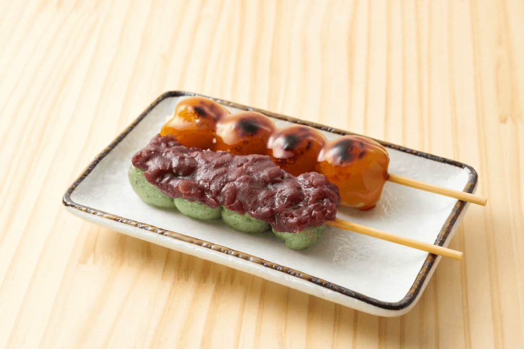Two skewers of odango, one green and one roasted. The roasted one has azuki bean paste smeared on it.