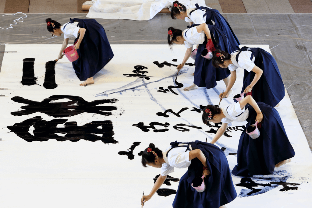 A bunch of shodo artists painting on a large paper together.