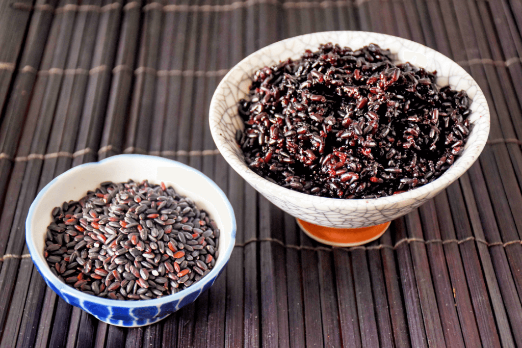 A bowl of cooked and uncooked purple rice.