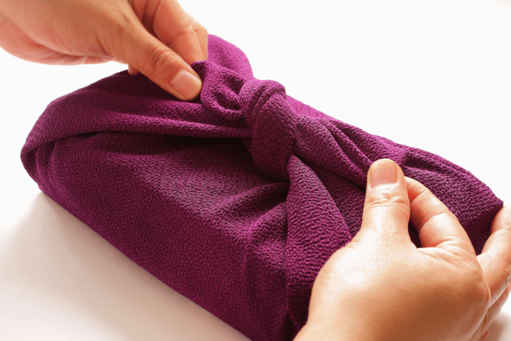 A person wrapping up a purple furoshiki.
