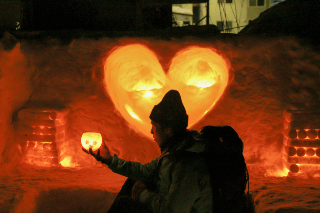 A person standing in front of an illuminated snow heart display at the Otaru Snow Light Path Festival.