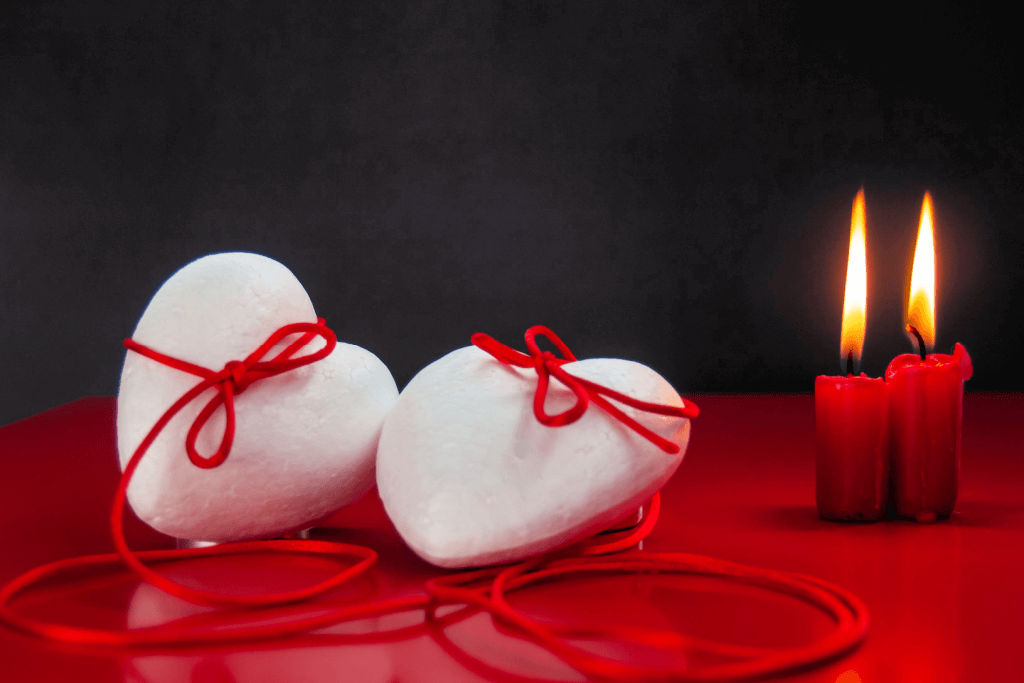 Two white hearts connected by the red thread of fate, with a couple of red candles in the background.