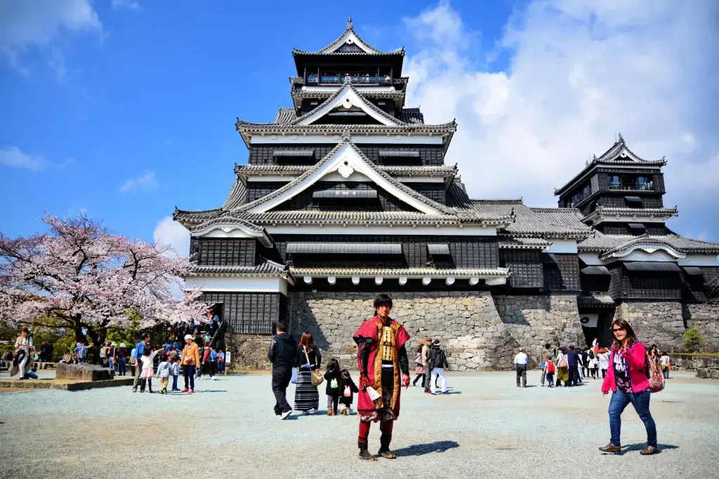 People hanging out at a castle during the spring. Some of them are dressed up as samurai.