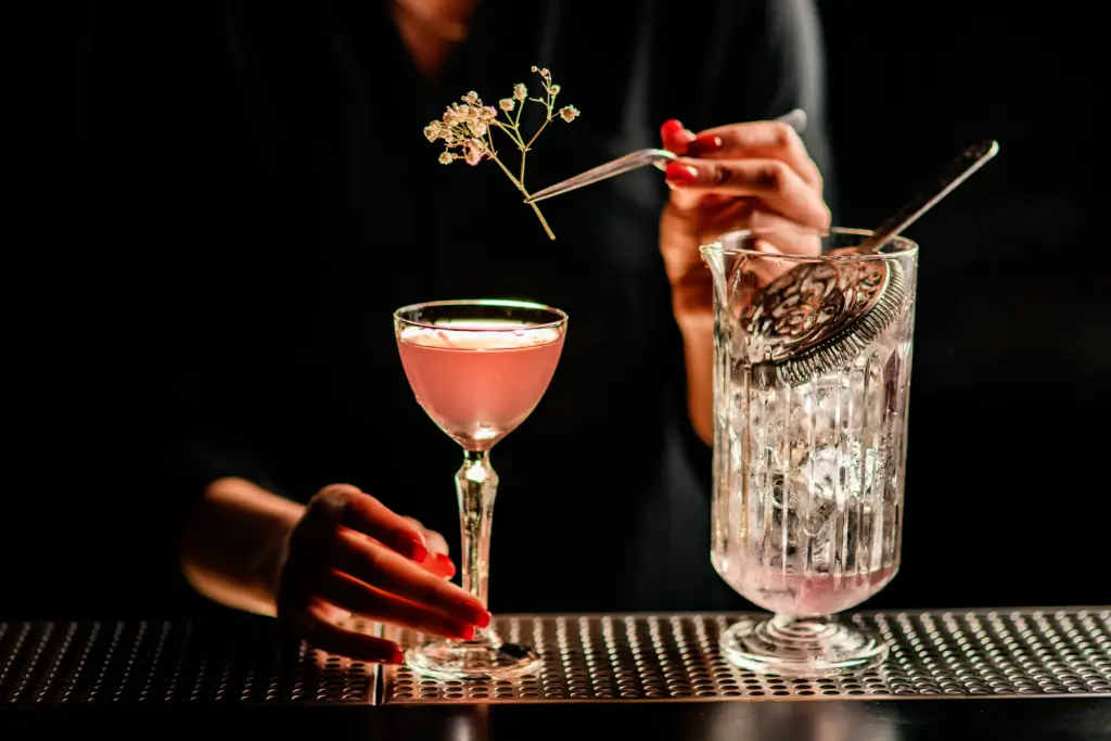 A person preparing a delicate pink cocktail in a luxury bar.