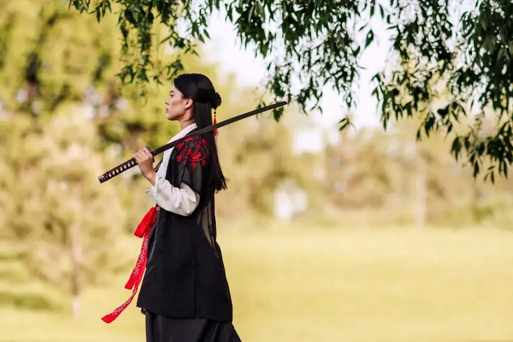A female warrior in all black, standing alone in a field.