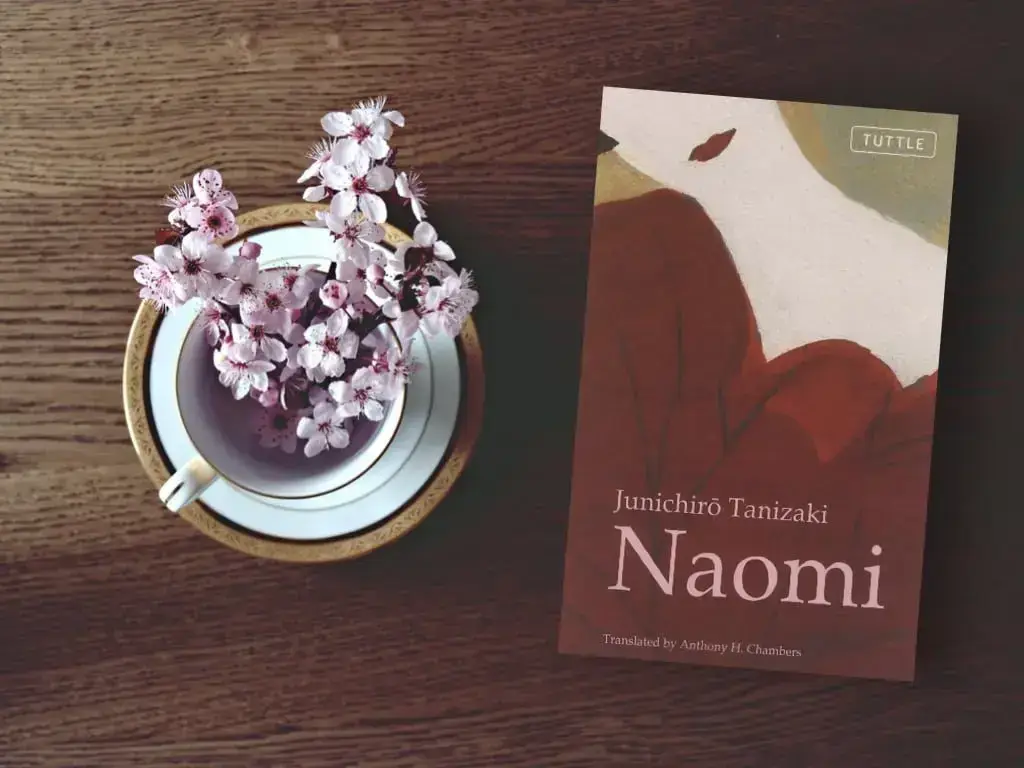 A copy of "Naomi" on a coffee table next to vase of flowers.