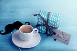 An assortment of Father's Day gifts, featuring a cup of coffee, a blue gift box and a mustache.