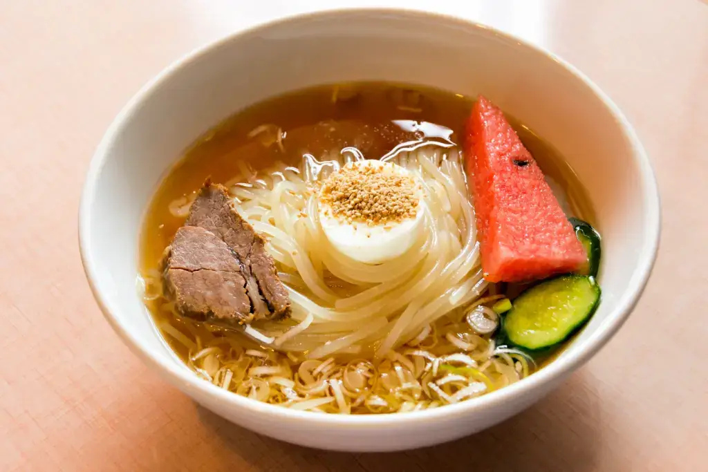 A bowl of Morioka Reimen which has beef and a slice of watermelon.