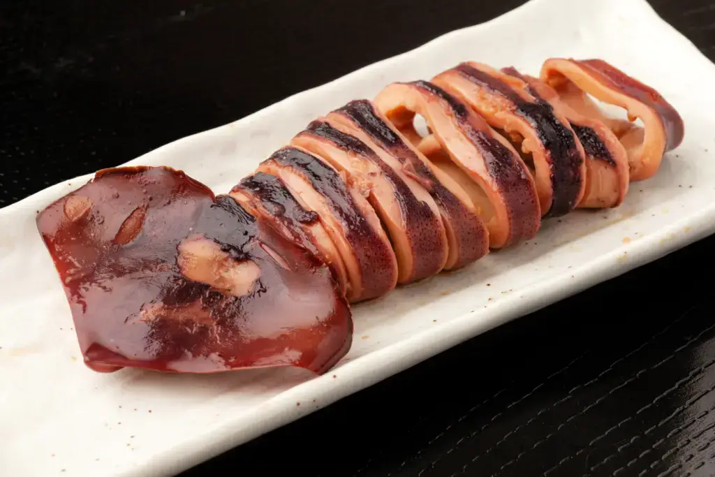 Chopped up ikayaki on a plate against a black background.