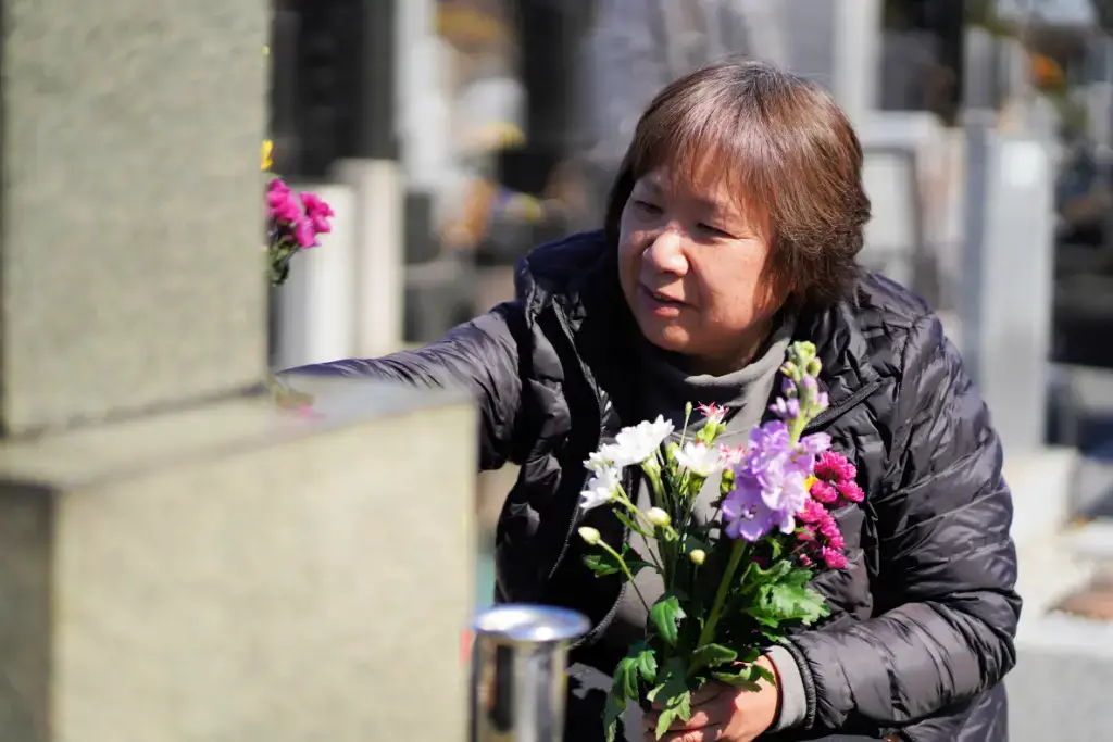 A woman with flowers visiting a grave during Obon season.