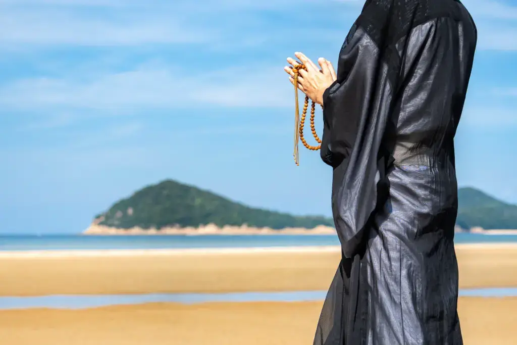 A Buddhist monk holding prayer beads at the beach.