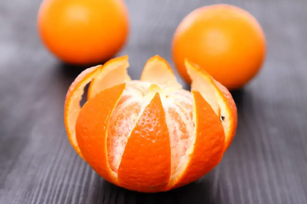 Three tankan citrus fruits. One of them is peeled in a star pattern.