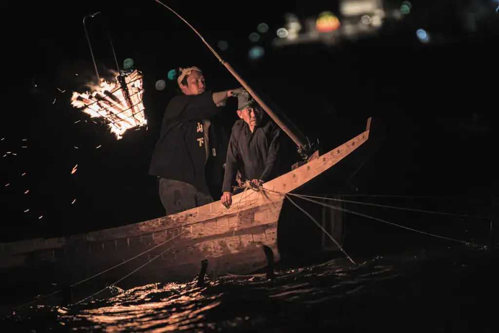 Two men fishing for sweetfish at night ukai style.