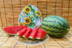 Slices of suika (watermelon) with a whole watermelon and a fan against a straw background.